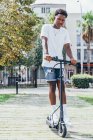 D'en bas homme sportif afro-américain chevauchant sur scooter électrique dans une journée nuageuse brillante — Photo de stock