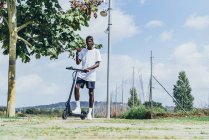Afro-Américain sportif équitation sur scooter électrique dans une journée nuageuse lumineuse — Photo de stock