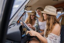Group of touristic charming ladies in hats studying map for navigation in trip in van — Stock Photo