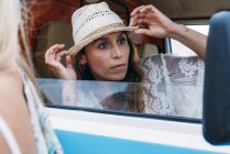 Приємна чарівна дама в капелюсі дивиться з посмішкою під час відкриття дверей автомобіля на пляжі — стокове фото
