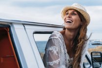 Piacevole signora affascinante in cappello distogliendo lo sguardo con il sorriso mentre si apre la porta della macchina sulla spiaggia — Foto stock