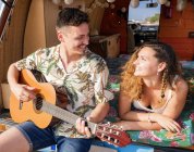 Allegra coppia tenera nel bagagliaio della macchina divertendosi insieme suonando la chitarra e godendo della musica — Foto stock