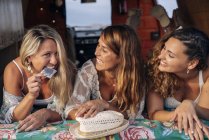 Joyful female friends discussing and showing condom while lying in trunk of car — Stock Photo