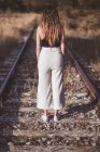 Femme aux cheveux longs debout sur les chemins de fer envahis d'herbe sèche — Photo de stock