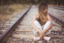 Длинноволосая женщина, сидящая на железной дороге, заросшая сухой травой — стоковое фото