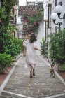 Обратный вид женщины в повседневном летнем платье с сумкой, идущей по улице Марбельи с итальянской собакой Грейхаунд на поводке — стоковое фото