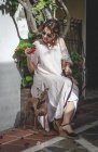 Позитивная женщина, сидящая на улице, держа цветы, держа собаку на поводке — стоковое фото