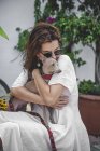 Glückliche Frau kuschelt Hund, während sie zusammen auf Zaun von Blumenbeet mit tropischen Pflanzen in Marbella ruht — Stockfoto