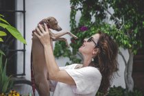 Щаслива жінка обіймає собаку, відпочиваючи разом на огорожі з тропічними рослинами у Марбельї. — стокове фото