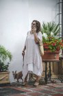 Ottimista donna felice alla moda che cammina per strada stretta a Marbella tenendo il cane levriero al guinzaglio mentre parla al telefono — Foto stock