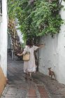 Back view of woman in casual summer dress with bag walking down in Marbella street with Italian Greyhound dog on leash — Stock Photo