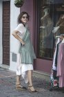 Seitenansicht der erfolgreichen selbstbewusst lächelnden fröhlichen Frau, die sich beim Einkaufen auf der Straße für ein gepunktetes Kleid entscheidet — Stockfoto