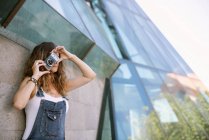 Junge enthusiastische Frau fängt den Moment ein, indem sie vor dem Hintergrund der Glasarchitektur mit der Kamera fotografiert — Stockfoto