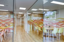 Світлий коридор з дерев'яною підлогою серед скляних стін світлих сучасних затишних офісних конференц-зони зі зручними помаранчевими та жовтими стільцями за великими дерев'яними столами — стокове фото