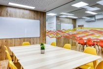 Diseño interior moderno de la oficina espaciosa luz zonificada por la pared de cristal con cómodas sillas amarillas y taburetes de barra gris en mesas de madera - foto de stock
