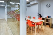 Corridoio luminoso con pavimento in legno tra pareti di vetro di luce moderno accogliente ufficio zone conferenze con comode sedie arancioni a grandi tavoli in legno — Foto stock