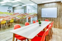 Design de interiores modernos de escritório espaçoso luz zoneada por parede de vidro com confortáveis cadeiras laranja e bancos de bar cinza em mesas de madeira — Fotografia de Stock