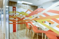 Світлий коридор з дерев'яною підлогою серед скляних стін світлих сучасних затишних офісних конференц-зони зі зручними помаранчевими стільцями за великими дерев'яними столами — стокове фото