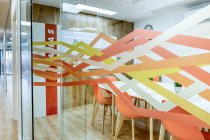 Light corridor with wooden floor among glass walls of light modern cozy office conference zones with comfortable orange chairs at big wooden tables — Stock Photo