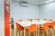 Design de interiores modernos de escritório espaçoso luz zoneada por parede de vidro com confortáveis cadeiras laranja e bancos de bar cinza em mesas de madeira — Fotografia de Stock