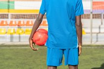 Black football player with ball standing on stadium — Stock Photo
