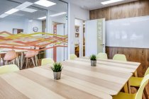 Design intérieur moderne de bureau spacieux et lumineux zoné par un mur de verre avec des chaises jaunes confortables et des tabourets de bar gris aux tables en bois — Photo de stock