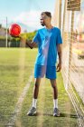 Schwarzer Teenager hält knallroten Ball auf Fußballplatz — Stockfoto