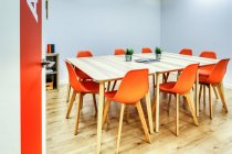 Modernes Interieur aus hellem, geräumigem Büro mit Glaswand, bequemen orangefarbenen Stühlen und grauen Barhockern an Holztischen — Stockfoto
