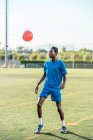 Чорний молодий чоловік жонглює футбольний м'яч на зеленому газоні — стокове фото