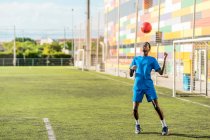 Magro nero adolescente giocoleria palla da calcio sulla testa sul campo verde — Foto stock