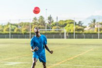 Magro adolescente preto malabarismo bola de futebol na cabeça no campo verde — Fotografia de Stock