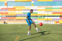 Етнічний підліток жонглює футбольний м'яч на зеленому полі — стокове фото