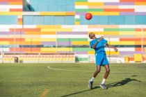 Афроамериканский подросток в синей форме, прыгающий яркий мяч на голове во время тренировки на футбольном поле — стоковое фото
