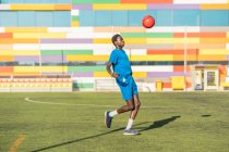 Atleta masculino étnico malabarismo bola de futebol no campo de esporte — Fotografia de Stock