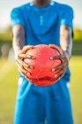 Руки черного футболиста в синей форме, несущего мяч — стоковое фото
