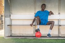 Чорний футболіст відпочиває на лавці на полі — стокове фото