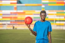 Adolescente negro con balón de fútbol contra asientos del estadio - foto de stock