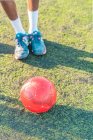 From above red ball placed on football field near sportsman in sneakers and socks during training — Stock Photo