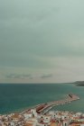 Вид з повітря на морський порт з щільно зупиненими будівлями з червоними дахами і пірсом з човнами на узбережжі з темною водою і сірим хмарним небом — стокове фото