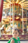 Child standing near moving carousel and dreaming at fair — Stock Photo