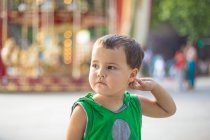 Child standing near moving carousel and dreaming at fair — Stock Photo