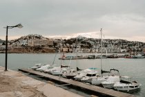 Sea port with white yachts and boats in city with buildings on hills with cloudy sky — Stock Photo