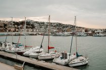 Sea port with white yachts and boats in city with buildings on hills with cloudy sky — Stock Photo