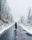 Seitenansicht eines Mädchens in schwarzer Jacke, das bei Schnee und trübem Winterwetter eine leere Landstraße überquert — Stockfoto