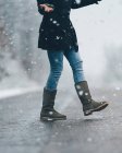 Coupe basse vue latérale de la jeune fille traversant la route de campagne vide sur la neige et le temps d'hiver sombre — Photo de stock