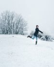 Vista laterale della donna che indossa vestiti caldi giocando con la neve sul campo invernale con le colline — Foto stock