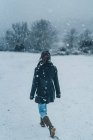 Vista posteriore della donna che indossa vestiti caldi camminando sul campo invernale con colline coperte di neve — Foto stock