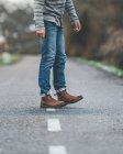 Male legs in jeans on country roadway on gloomy cloudy weather — Stock Photo