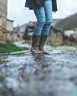 Female traveler in jeans and brown boots jumping on wet trail in autumn weather — Stock Photo