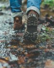 Back view of male traveler brown boots walking on wet trail in autumn forest — Stock Photo